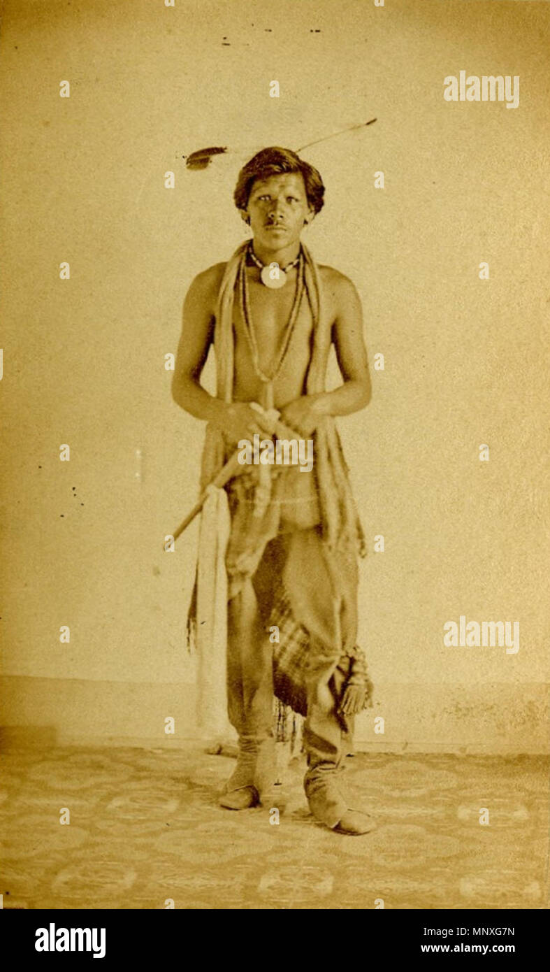Portrait of a Native North American man . Photograph (black and white) carte de visite; studio portrait of a Native North American man standing, wearing two eagle feathers in his hair, a dentalium necklace, an additional necklace, a cloth garment draped around his neck, a pair of leggings, a leg ornament on his left knee, a blanket wrapped around his waist, a pair of moccasins, and holding a tomahawk; Omaha(?), United States of America. 1860s.   1148 Studio portrait of a Native North American man Stock Photo