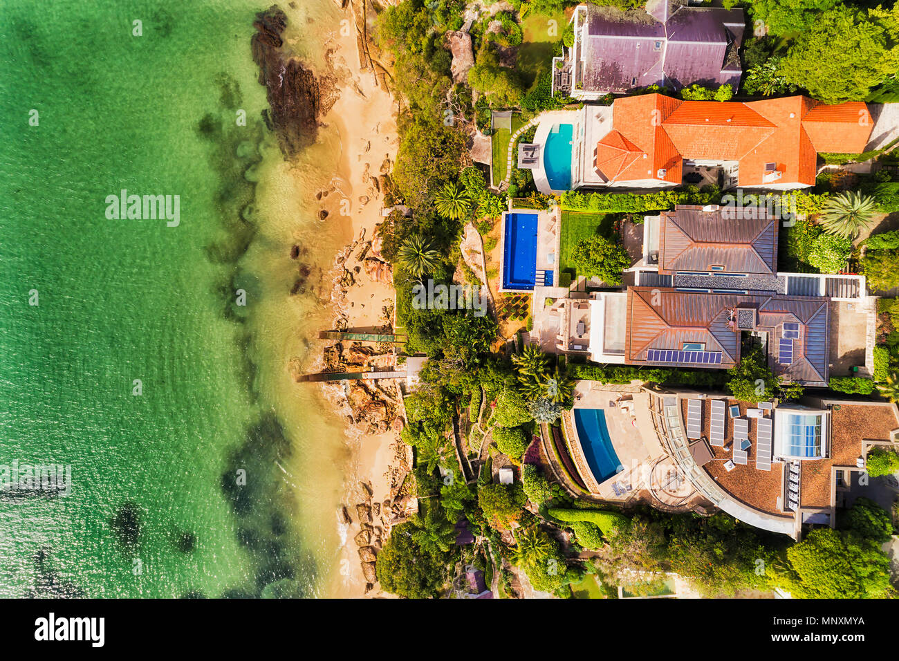 Wealthy residential houses on Sydney Middle Harbour waterfront touching cleand remote sandy beach in aerial overhead view on a sunny bright day. Stock Photo