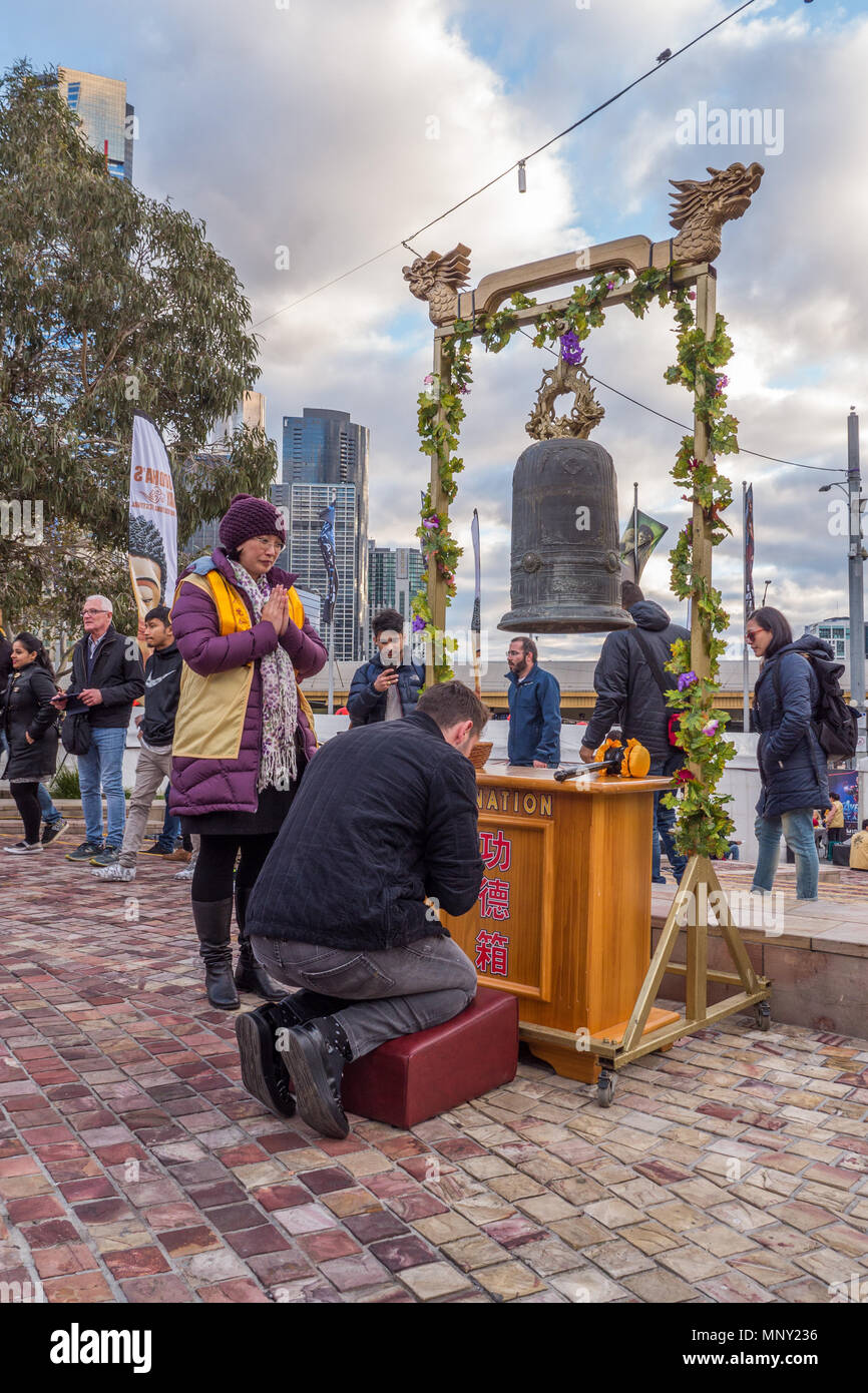 Middle aged man with hands clasped in prayer head bowed in front of large brass bell at Buddha Birthday festival in Melbourne Australia. Stock Photo