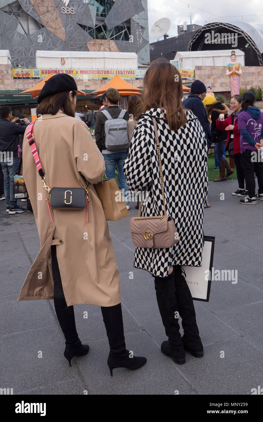 Two young Asian women dressed in very expensive designer coats black boots and designer handbags watching people at Buddhist festival. Stock Photo