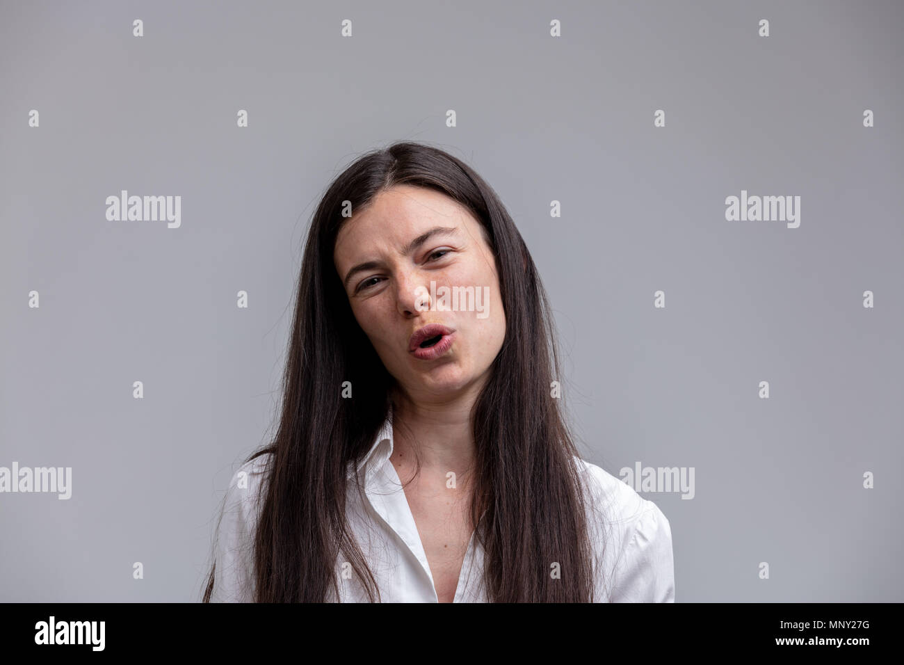 Scornful attractive woman talking to the camera as she jeers at the viewer with a derisory expression and frown over grey with copy space Stock Photo