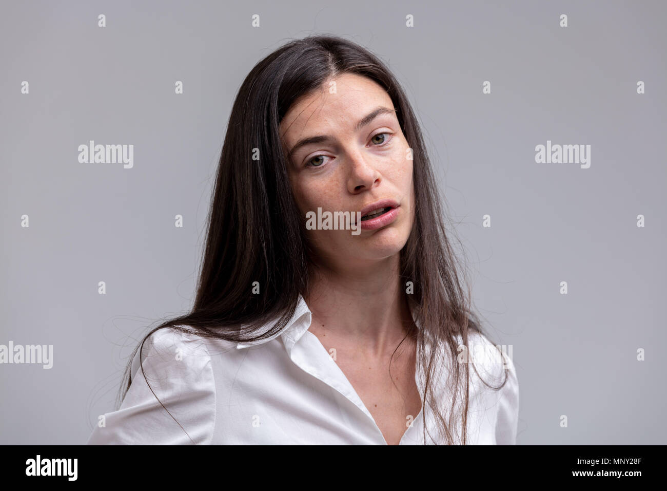 Sympathetic genuine young woman speaking to the camera with titled head and look of empathy over a grey background Stock Photo