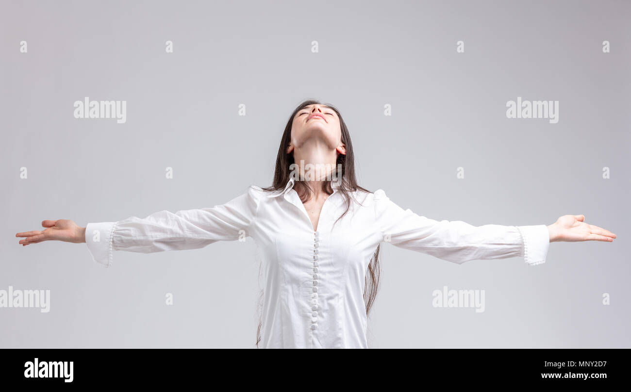 Young woman enjoying a moment of peace standing with outstretched arms and closed eyes with a serene expression and head tilted back over grey Stock Photo