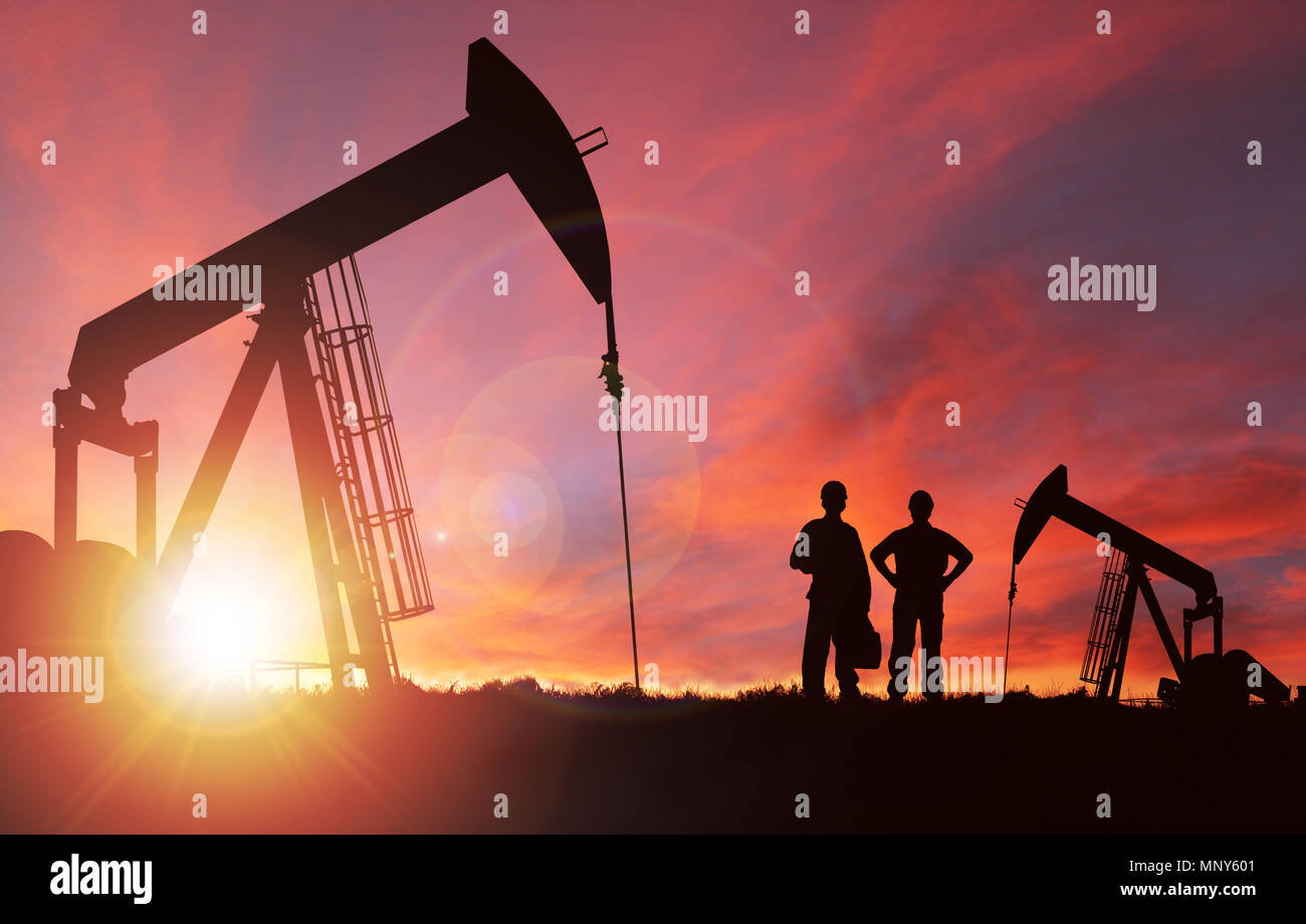Pump jack silhouette and hard hat workers against a sunset sky with deliberate lens flare and copy space. These jacks can extract between 5 to 40 litr Stock Photo