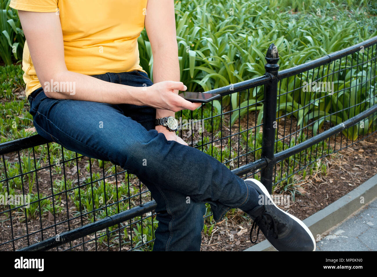 young man in blue jeans and yellow t shirt using his cellphone Stock Photo