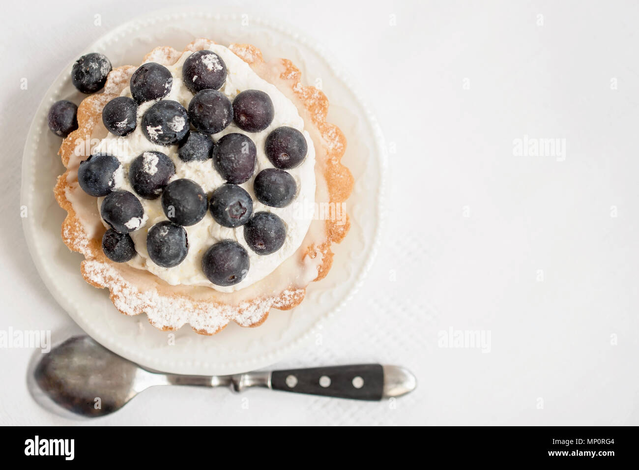 Fresh blueberry tart in portion plate, next to a spoon, white napkin. Delicious summer berry dessert. Top view, copy space for text, background Stock Photo