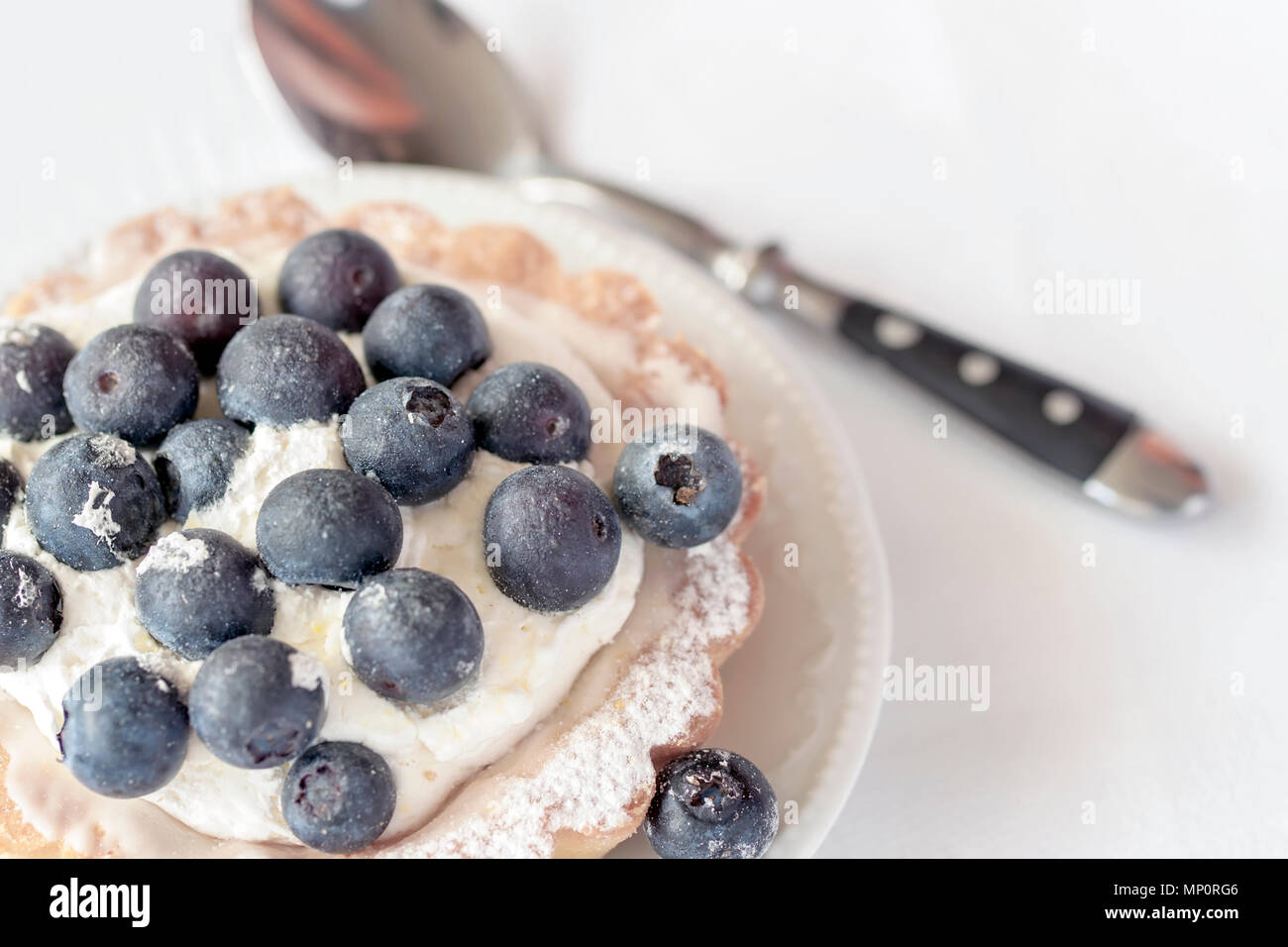 Fresh blueberry tart in portion plate close-up and spoon, white napkin. Delicious summer berry dessert. Top view Stock Photo