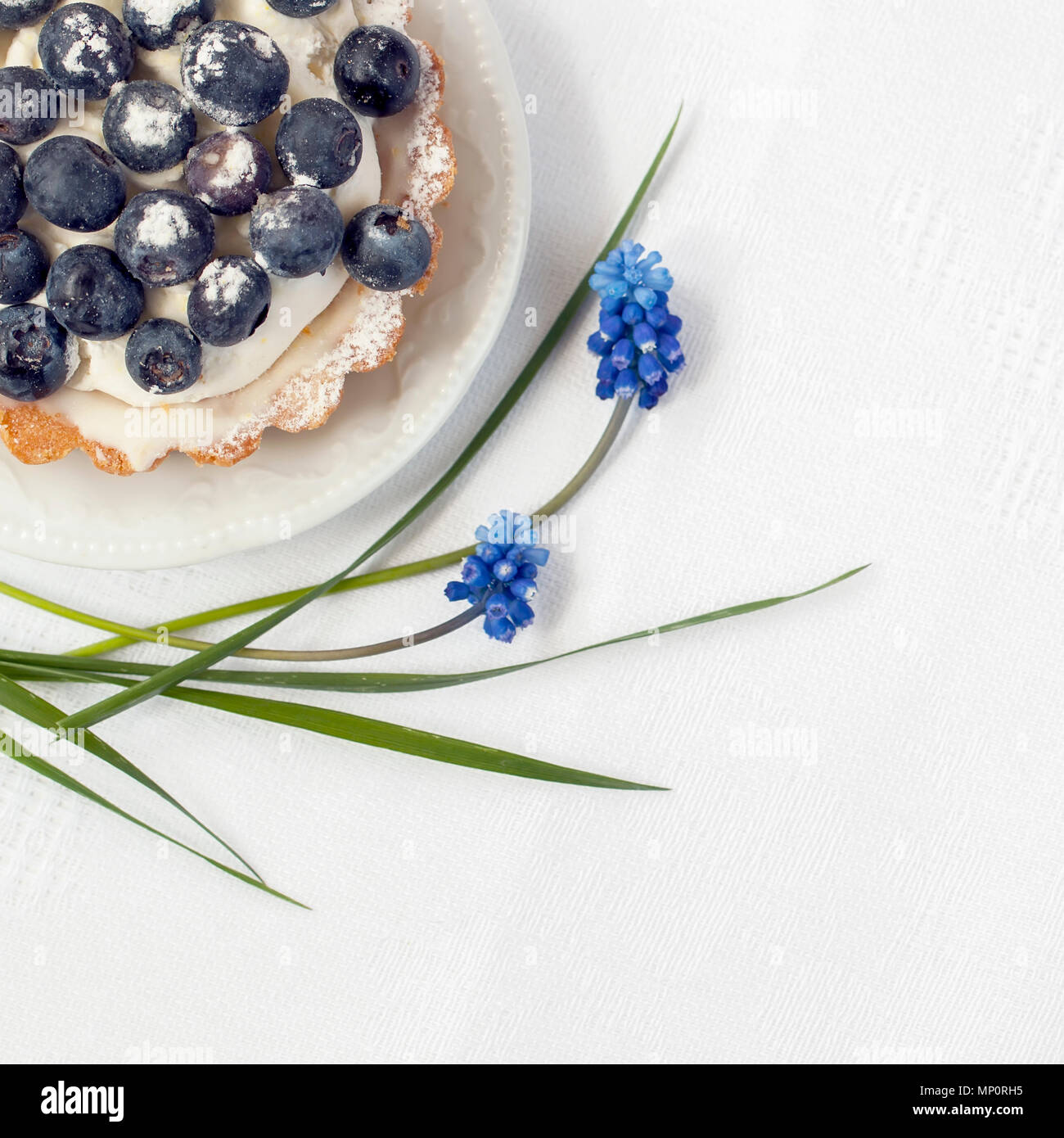 Fresh blueberry pie with vanilla custard in portion plate close-up, next to elegant blue flowers, , white napkin. Delicious and romantic summer berry dessert, copy space Stock Photo