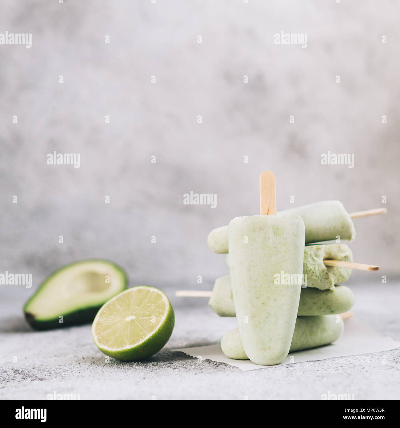 Homemade raw vegan avocado lime popsicle. Sugar-free, non-dairy green ice cream on gray cement textured background. Copy space. Ideas and recipes for healthy snack, dessert or smoothie Stock Photo