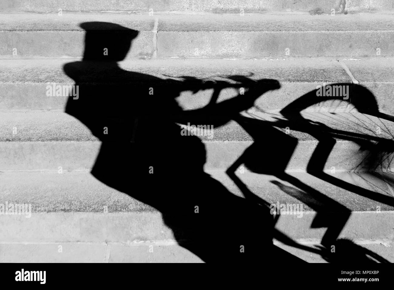 Blurry abstract  shadow of a cyclist with a helmet on , pushing his bike up the public city stairs in black and white Stock Photo