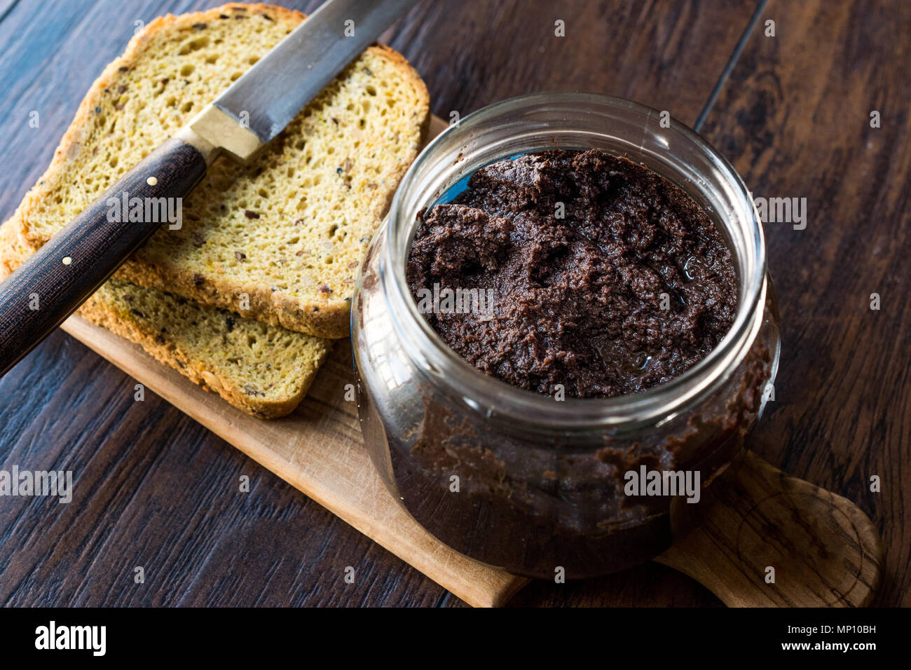 Black Olive Tapenade in Jar with Knife and Bread. Organic Food. Stock Photo