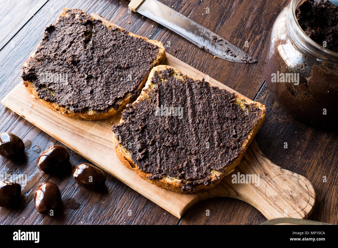 Black Olive Tapenade on Bread with Knife and Jar. Organic Food. Stock Photo