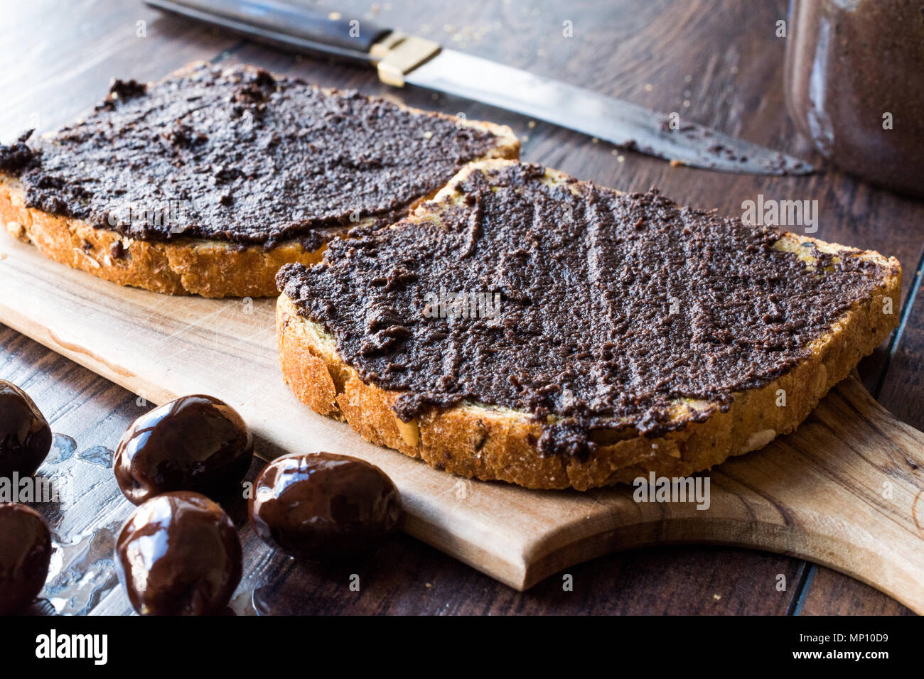 Black Olive Tapenade on Bread with Knife and Jar. Organic Food. Stock Photo