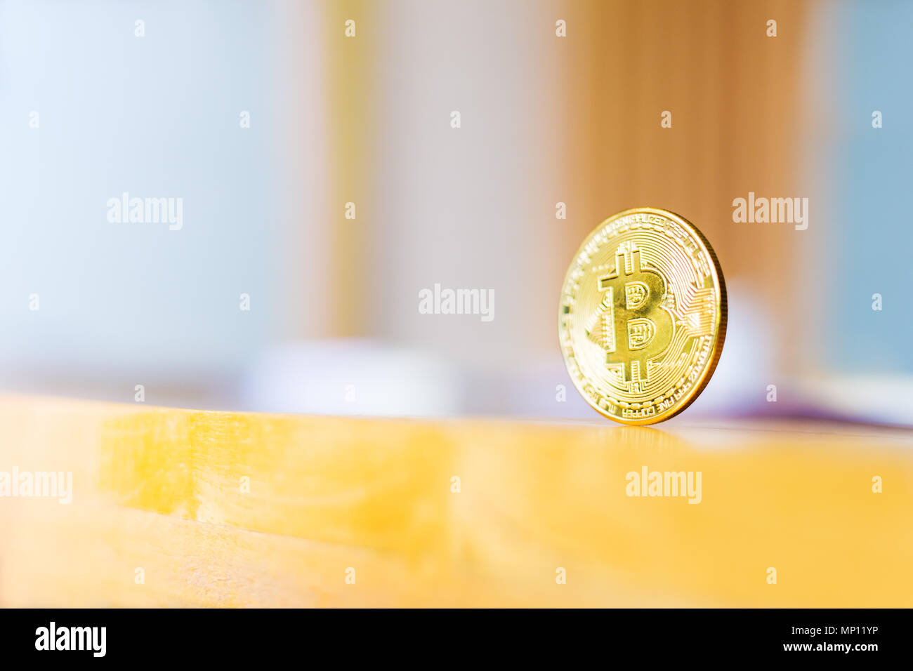 A shiny golden color Bitcoin, cryptocurrency coin, standing on wood table,  reflecting the light, against blurred office background, good for cryptocur  Stock Photo - Alamy
