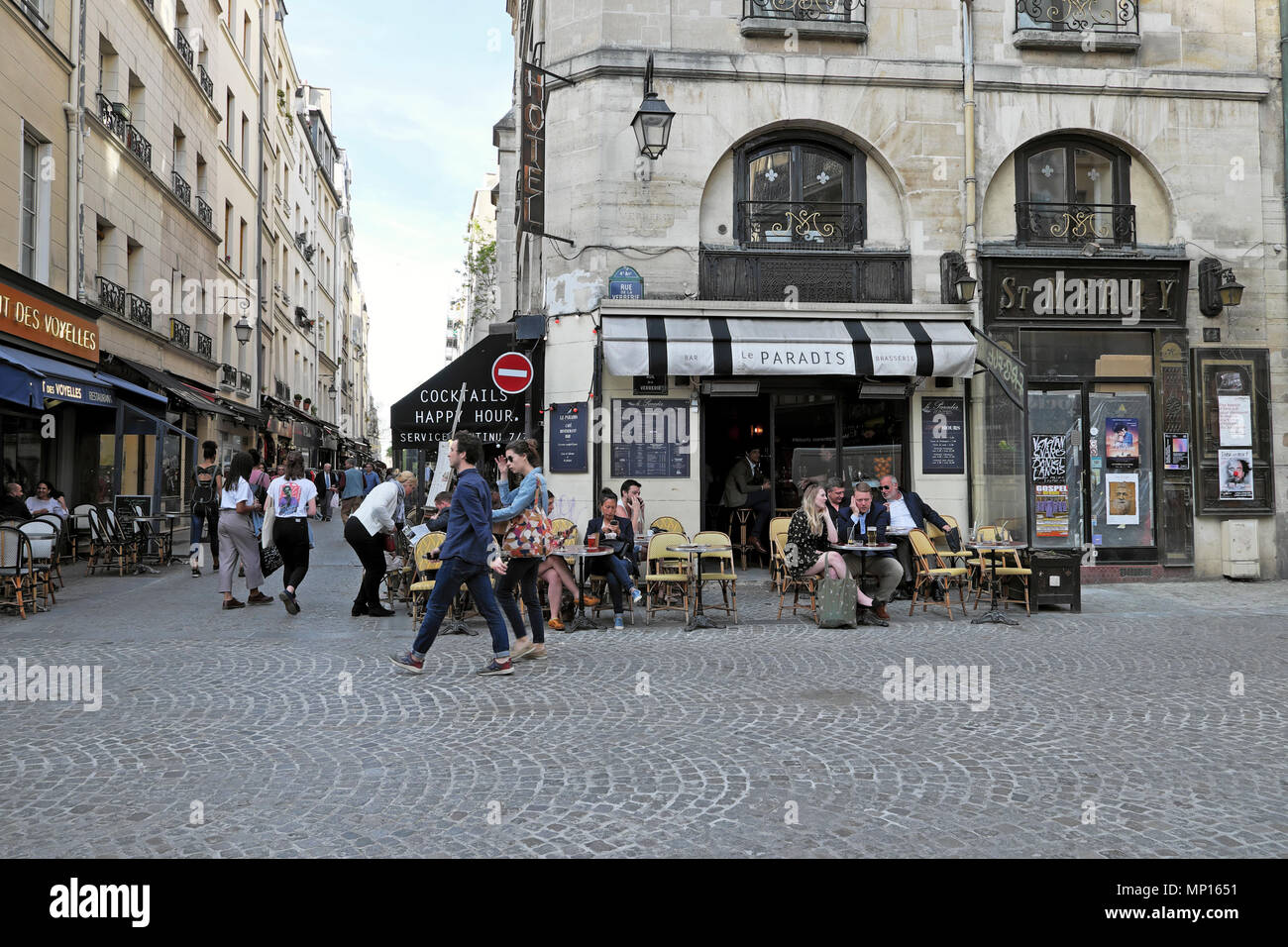 Couple walking by people sitting at tables outside Le Paradis on corner of  Rue de la Verrerie & Rue Saint-Martin Paris France Europe EU KATHY DEWITT Stock Photo