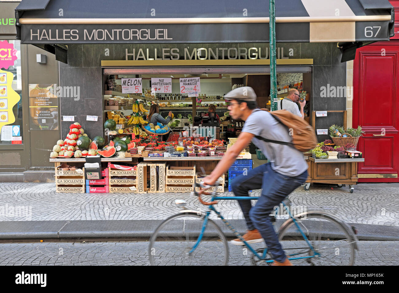 Cyclist riding bike along the Rue Montorgueil street past Halles Montorgueil fruit and vegetable shop in Paris France Europe EU  KATHY DEWITT Stock Photo