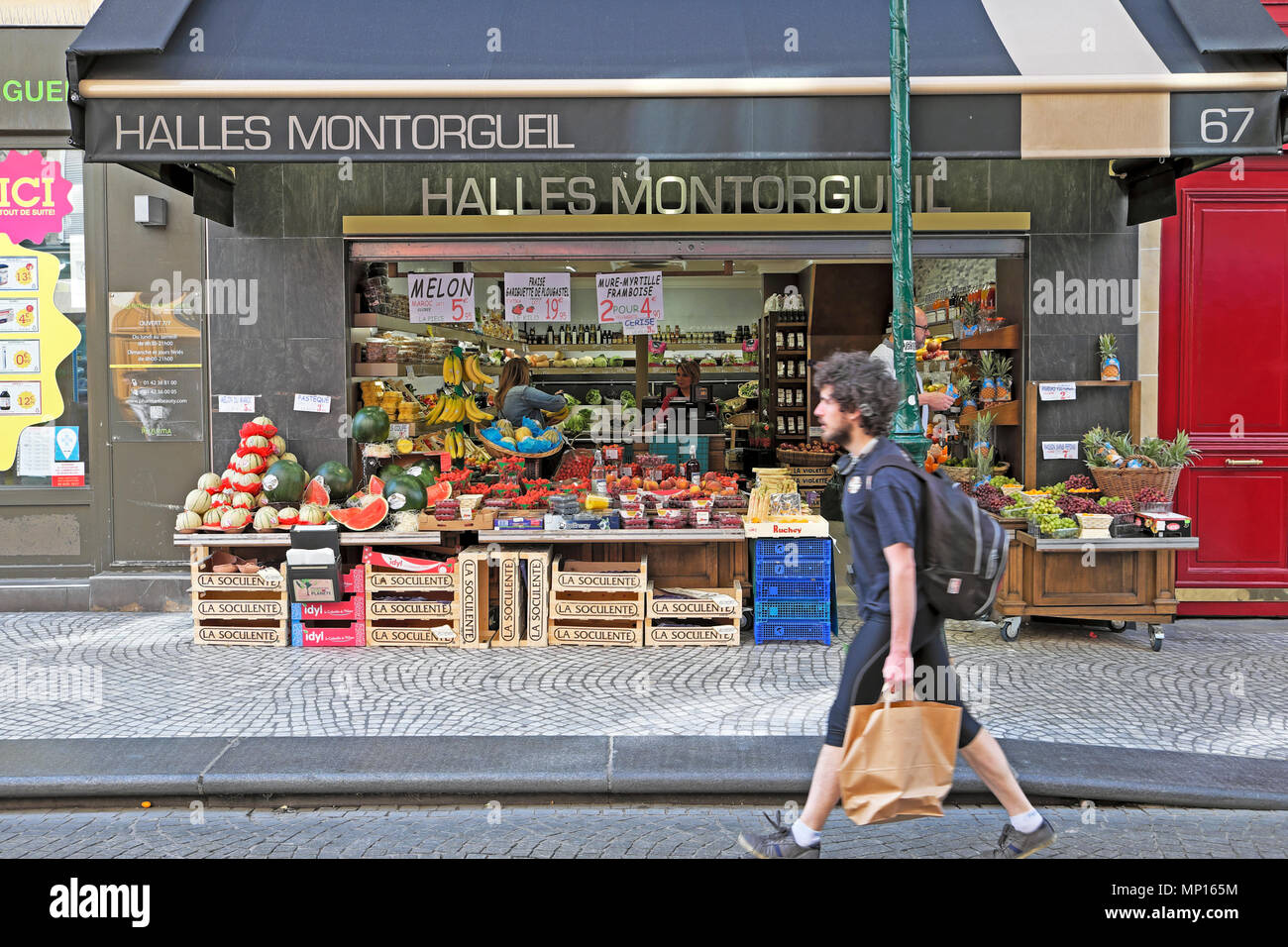 Man with shopping bag walking along Rue Montorgueil street past Halles Montorgueil fruit and vegetable shop in Paris France Europe EU KATHY DEWITT Stock Photo