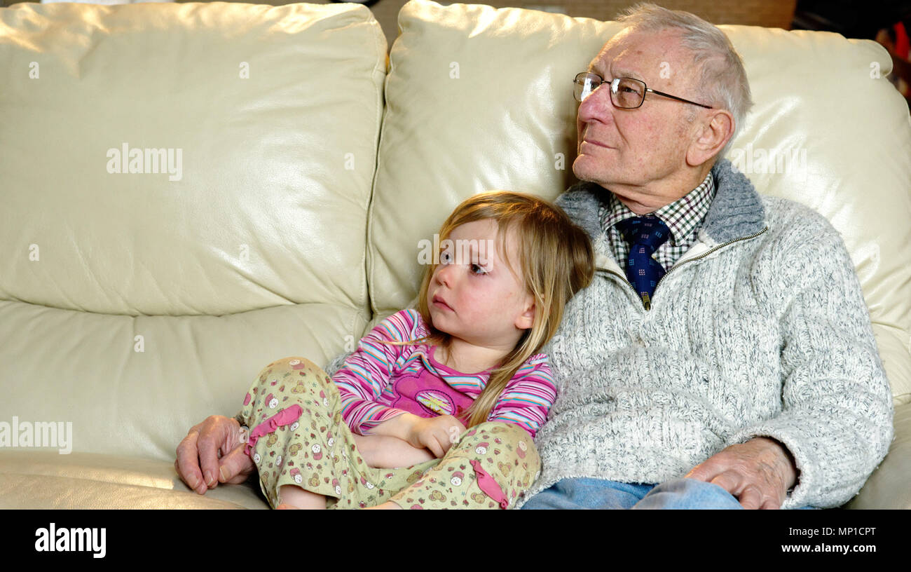 Grandfather and his 3 yr old grand-daughter watching TV together Stock Photo