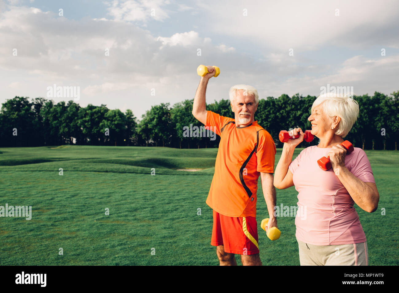 senior man and woman working out with dumbbells in a park at sunny day Stock Photo