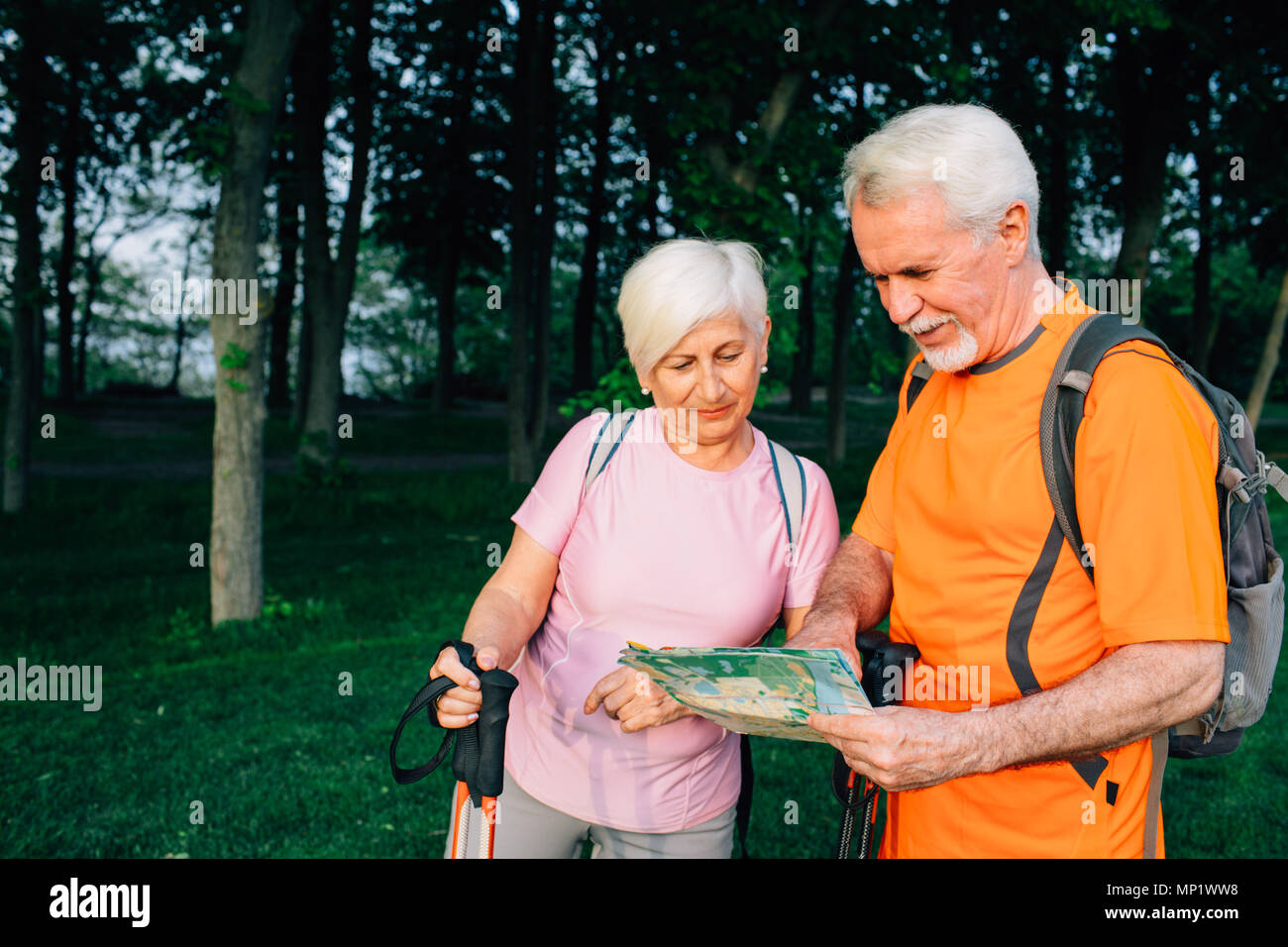 Senior couple checking map, standing with trekking poles at forest. retirement, travel and active lifestyle of the elderly people Stock Photo
