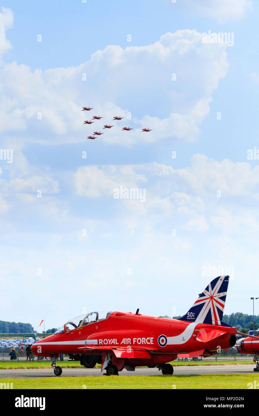 The Red Arrows Aerobatic display team BAE Hawk jet on the tarmac while the rest of the team fly overhead. RAF Waddington, Lincolnshire, England Stock Photo