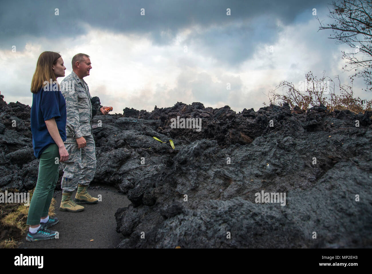 FEMA employee Meghan Breitenbach and U.S. Air Force Lieutenant Colonel Chuck Anthony view a portion of the hardened lava flow spewing from the Kilauea volcanic eruption May 18, 2018 in Pahoa, Hawaii. The recent eruption continues destroying homes, forcing evacuations and spewing lava and poison gas on the Big Island of Hawaii. Stock Photo