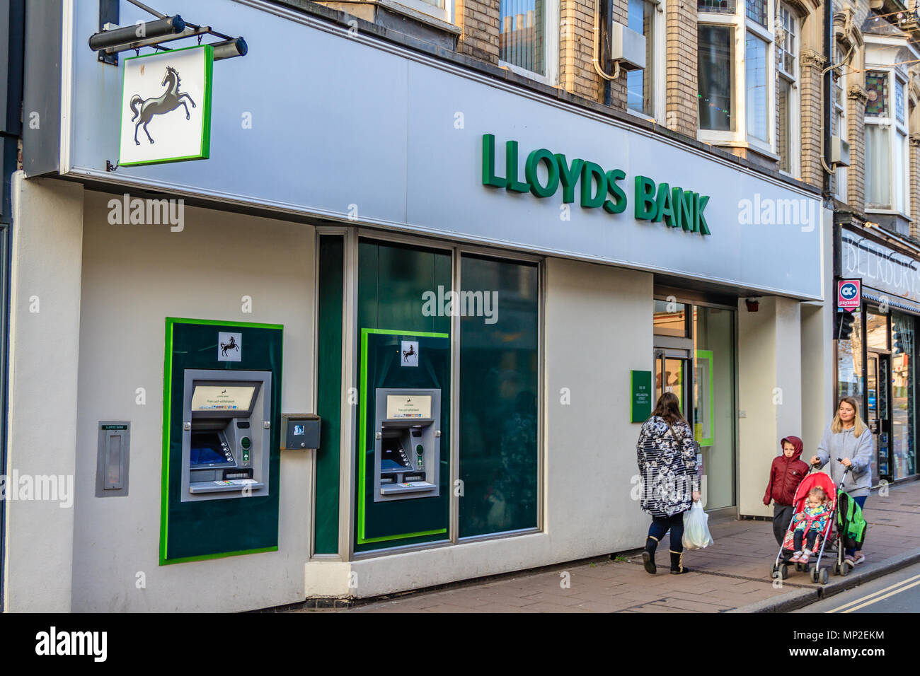 Woman with pushchair and boy walking past the outside of a high street Lloyds Bank, Teignmouth, Devon. Feb 2018. Stock Photo