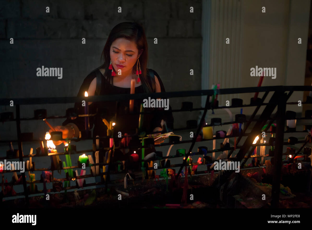 Attractive, upscale Filipino Asian woman lights votive candles in a Catholic church in the Philippines. Stock Photo
