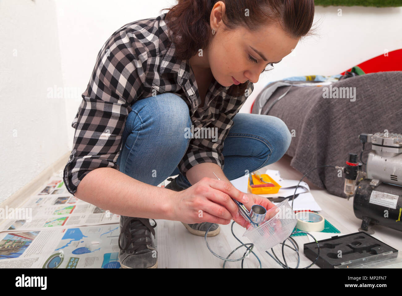 Close-up of a woman artist in jeans cleans and prepares the airbrush for the work of painting the walls. Stock Photo