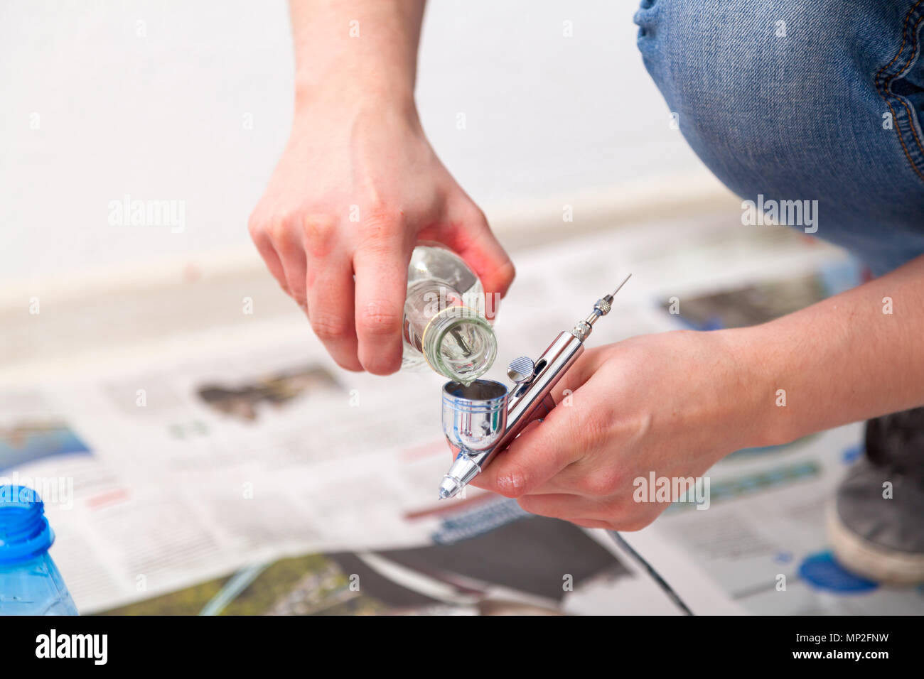 Close-up of a woman artist in jeans and sneakers washed with water and prepares a metal airbrush for work before painting the walls in the children's  Stock Photo