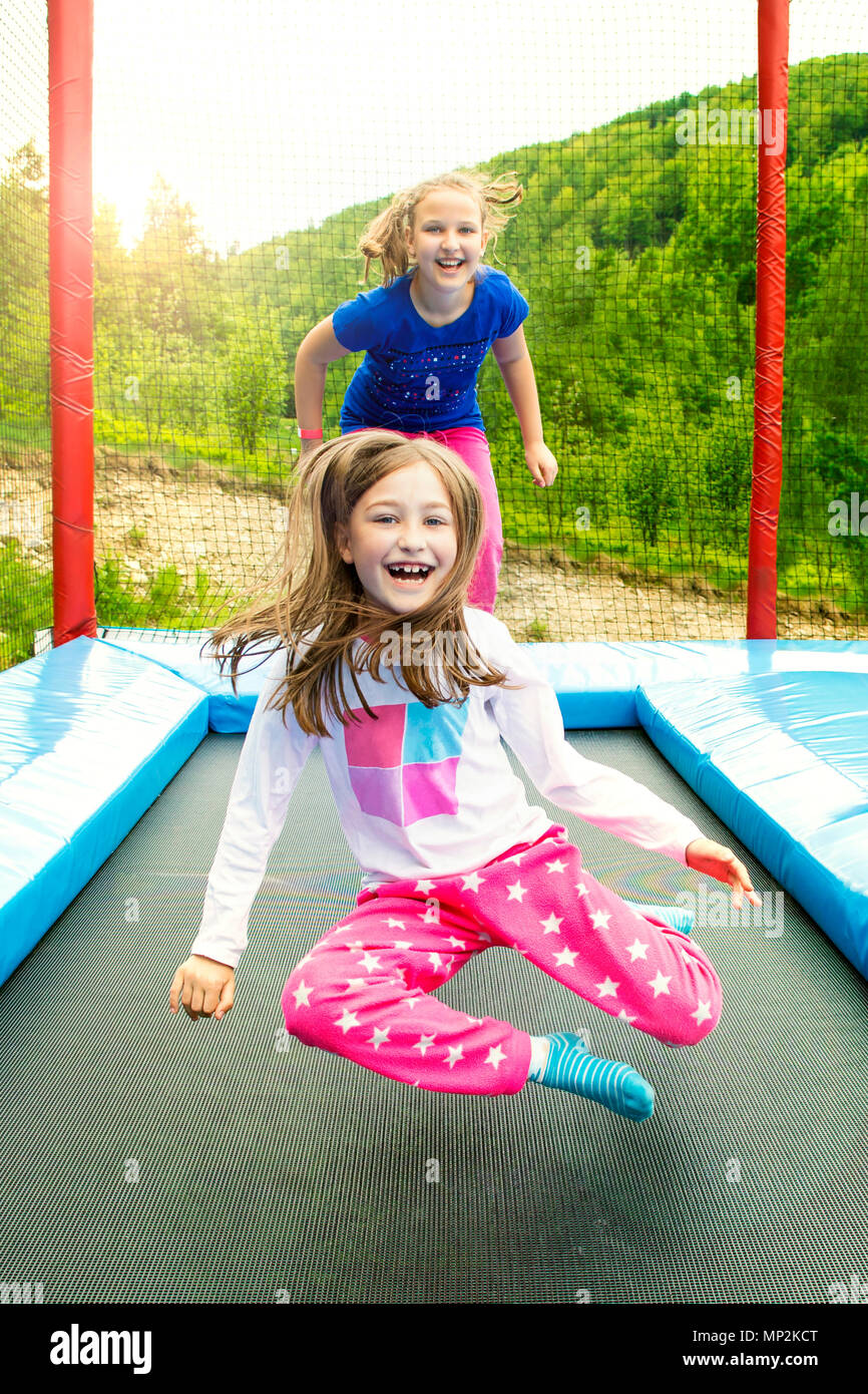 Happy girls jumping high on a trampoline on a sunny day outdoors. Stock Photo