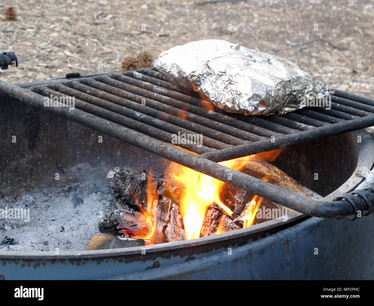 Mountain Camp Fire Cooking Foil Dinners on Grate Over Hot Pit Stock Photo