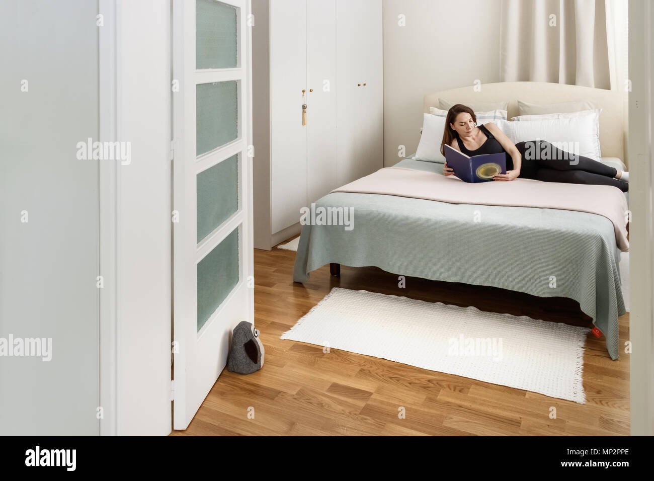 Portrait of a woman reading a book laying down on her bedroom, natural light. Stock Photo