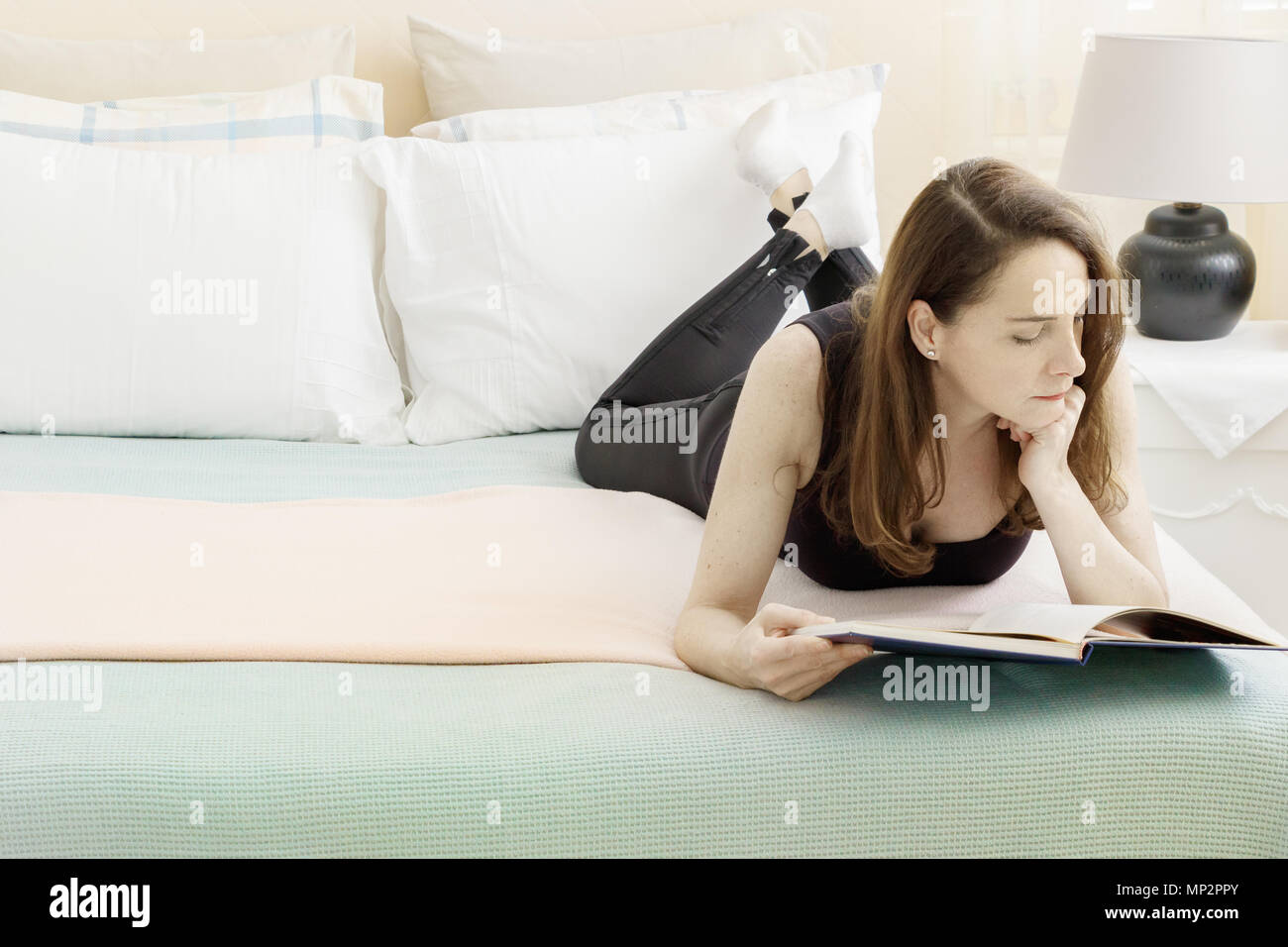Portrait of a woman reading a book laying down on her bedroom, natural light. Stock Photo