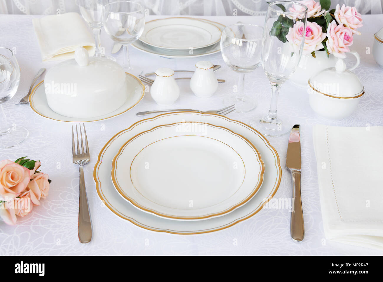 Beautifully decorated table with white plates, glasses, cutlery and flowers on luxurious tablecloths Stock Photo