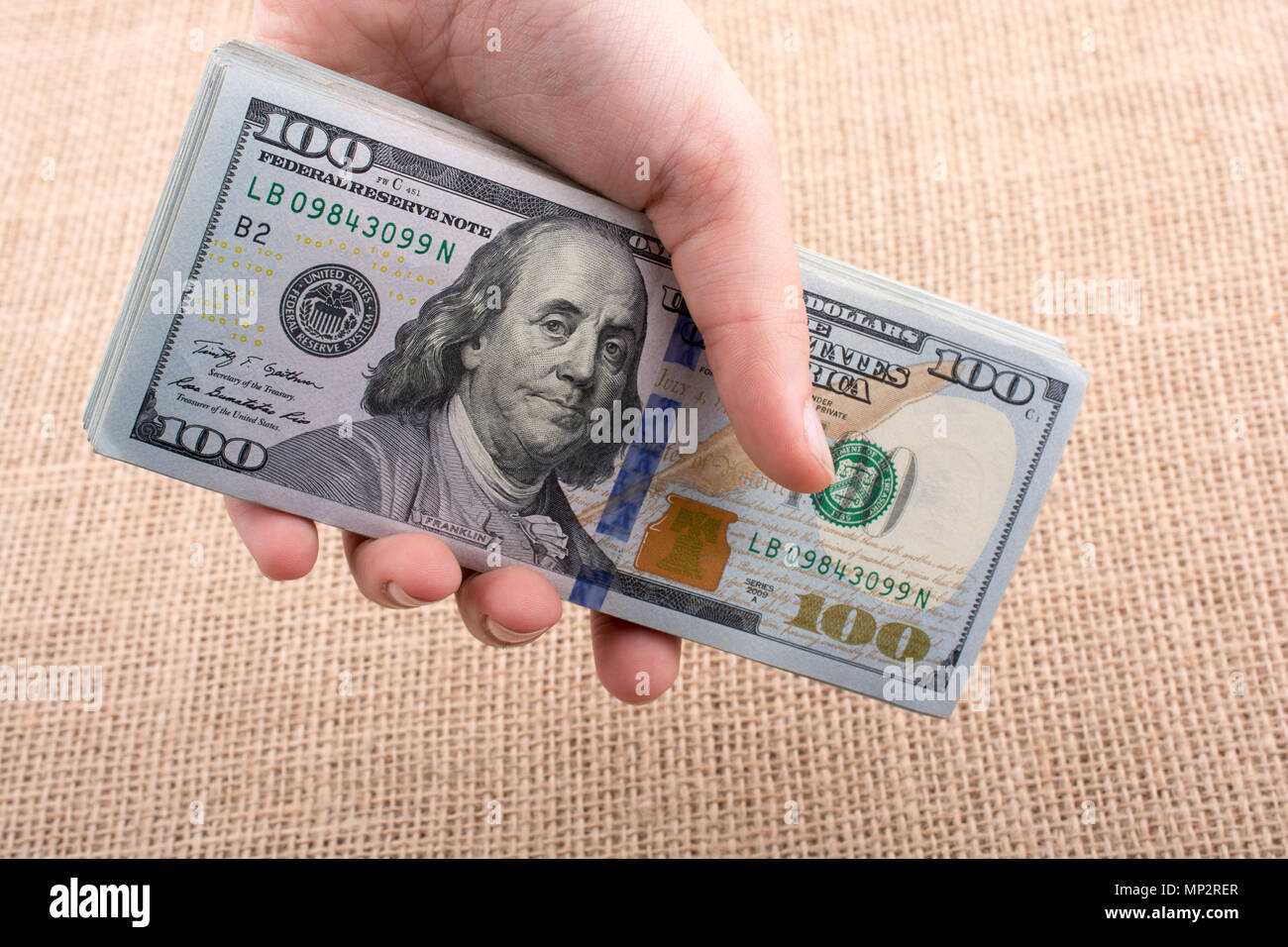 Hand holding banknote bundle of US dollar on a linen canvas background ...