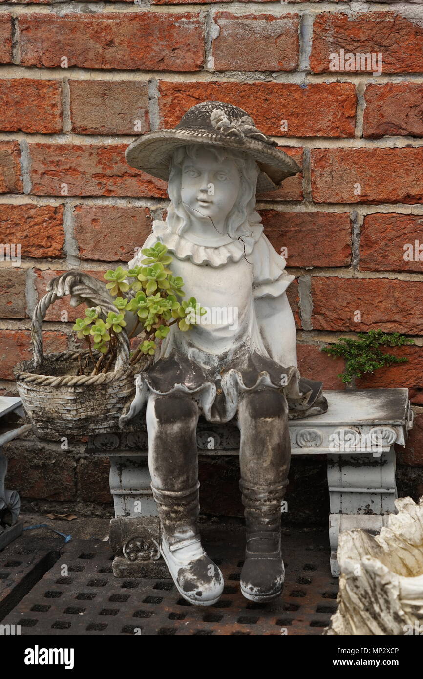 Statue of A Girl And Her Basket Setting In Front Of A Brickwall Stock Photo