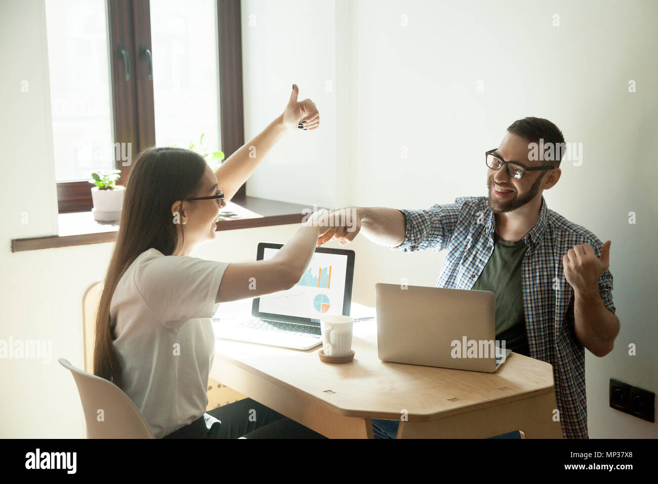 Smiling freelancers giving fists bump and showing thumbs up Stock Photo