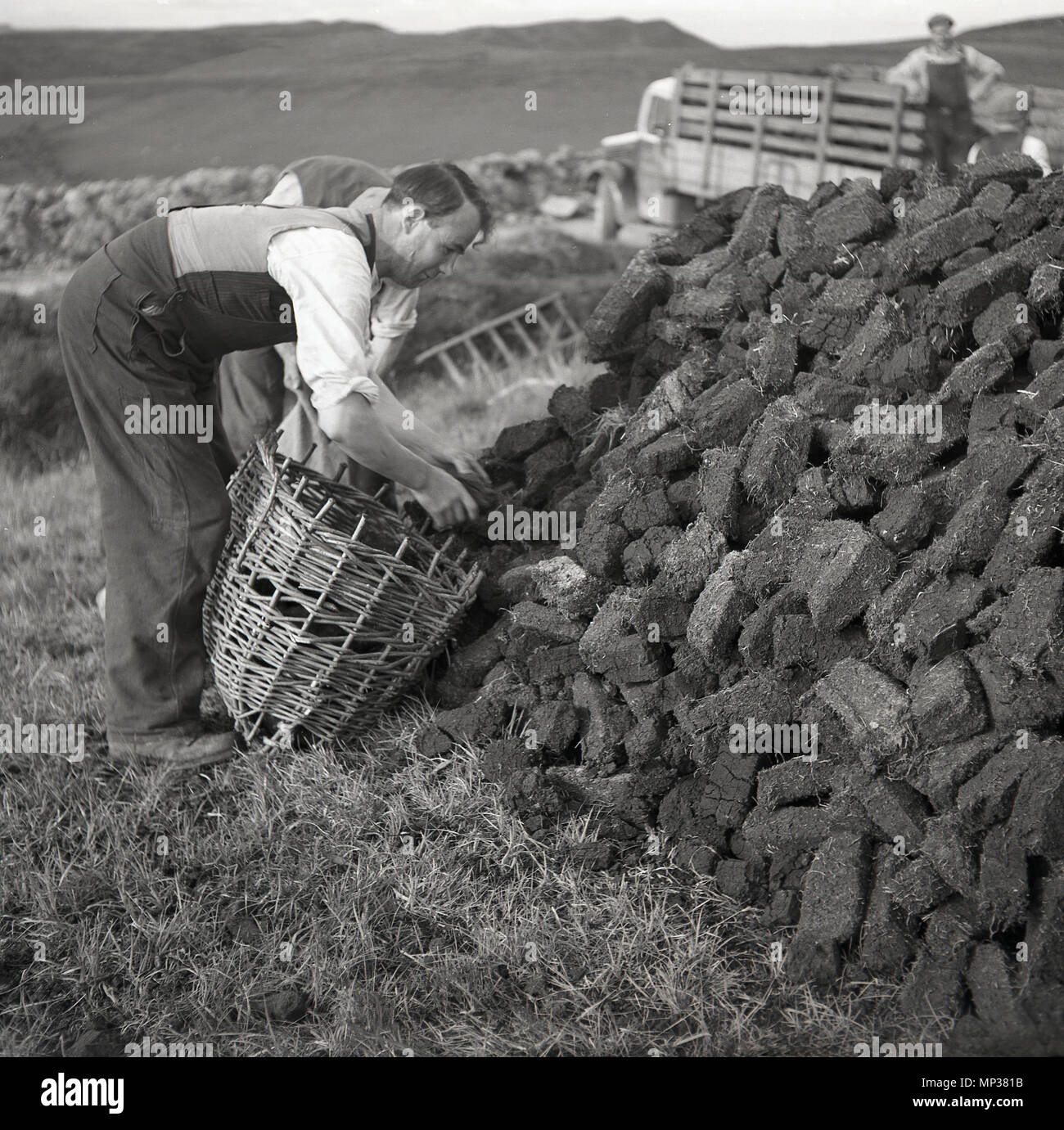 1950s, two men putting cut turf or peat from a stack, into wicker