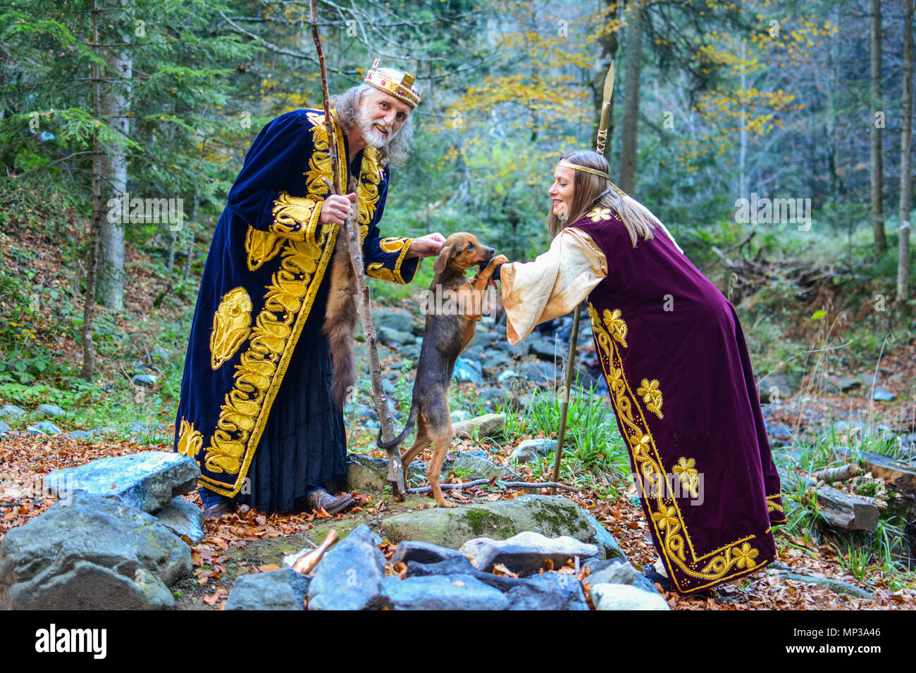 The old king, a queen having funwith small hunting dog outdoors in colourful autumn forest Stock Photo
