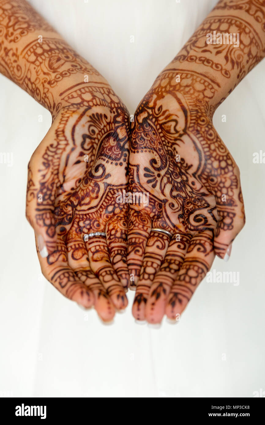 Mehandi bride's hands against white wedding dress Stock Photo