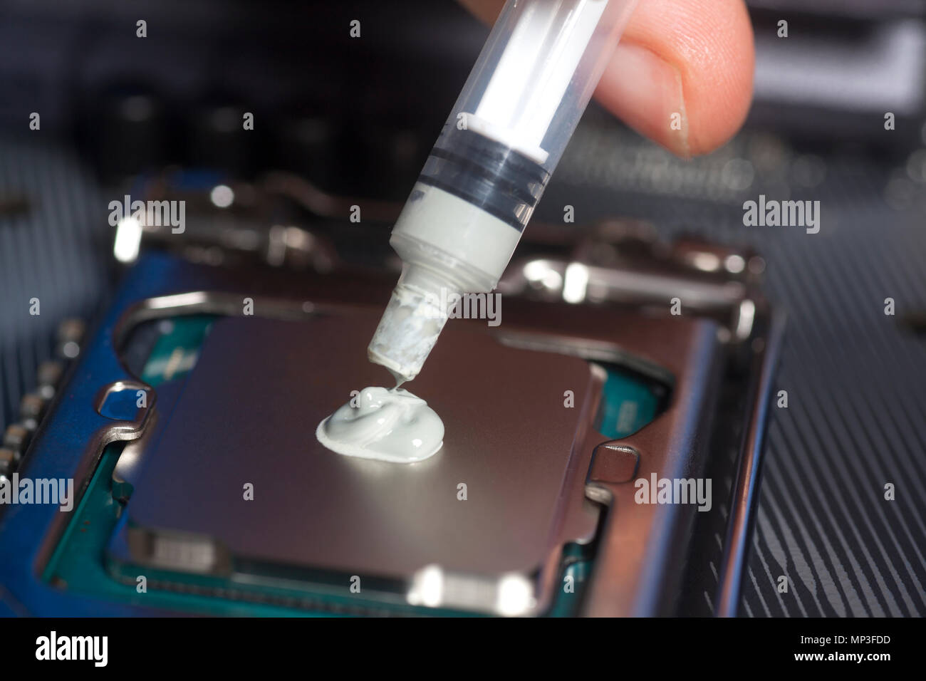 Hand with syringe applying thermal paste on the CPU processor on motherboard Stock Photo
