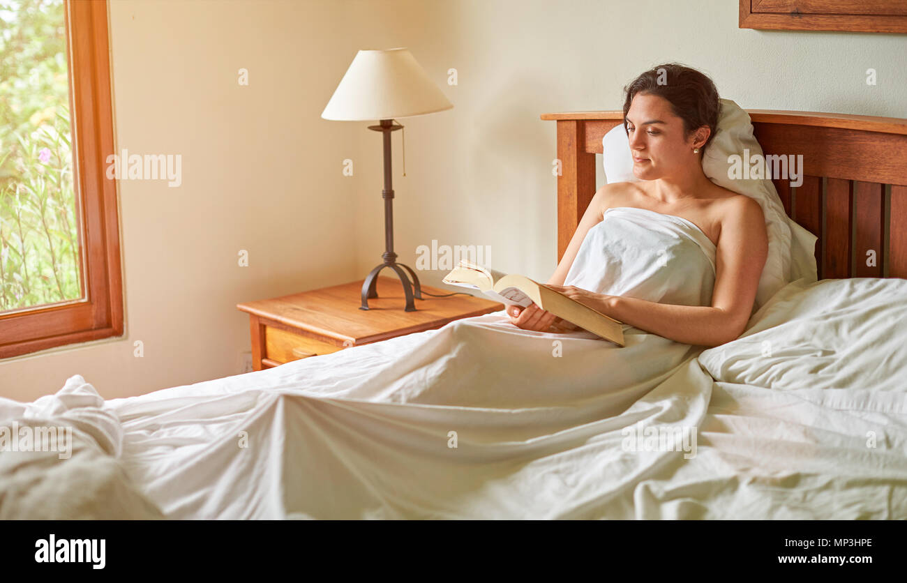 Girl reading big book in bed. One woman with book in bedroom Stock Photo