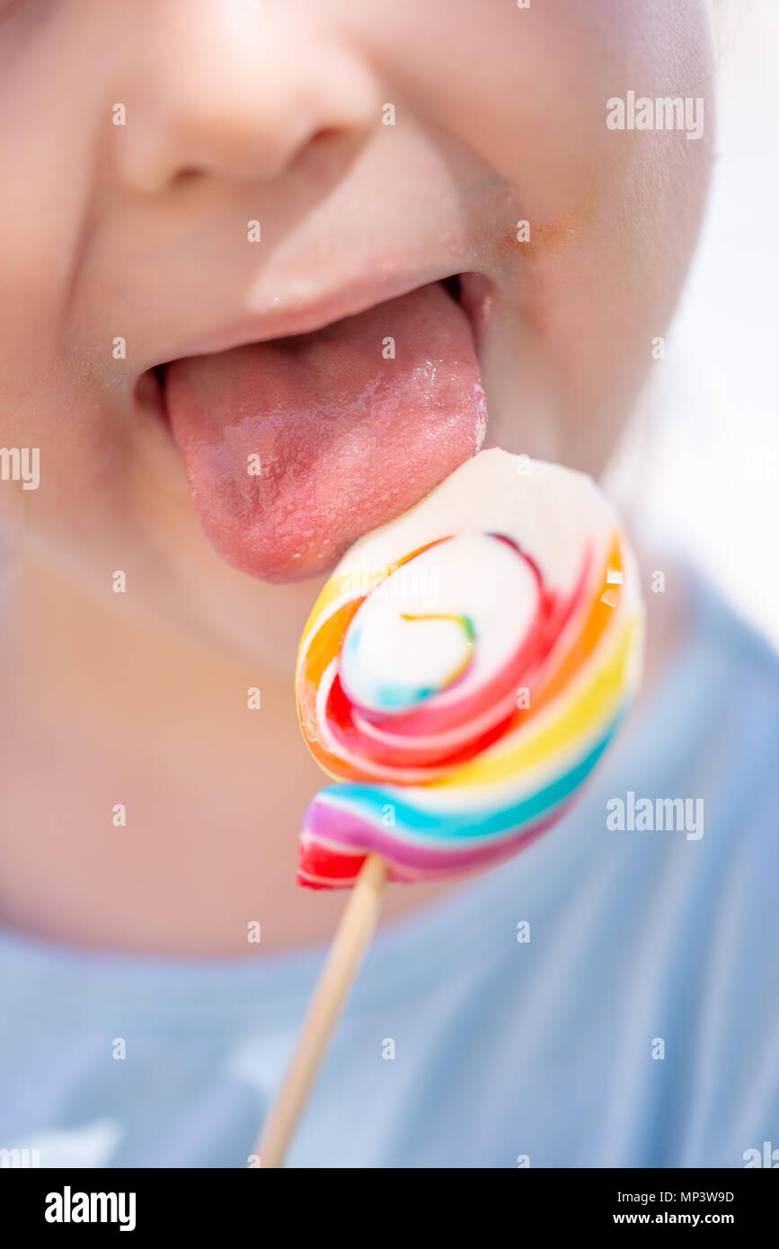 Little kid, child with colorful lolipop, licking on the lolipop, unrecognizable Stock Photo