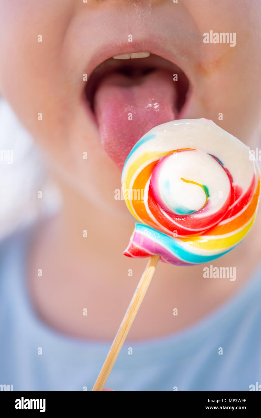 Little kid, child with colorful lolipop, licking on the lolipop, unrecognizable Stock Photo