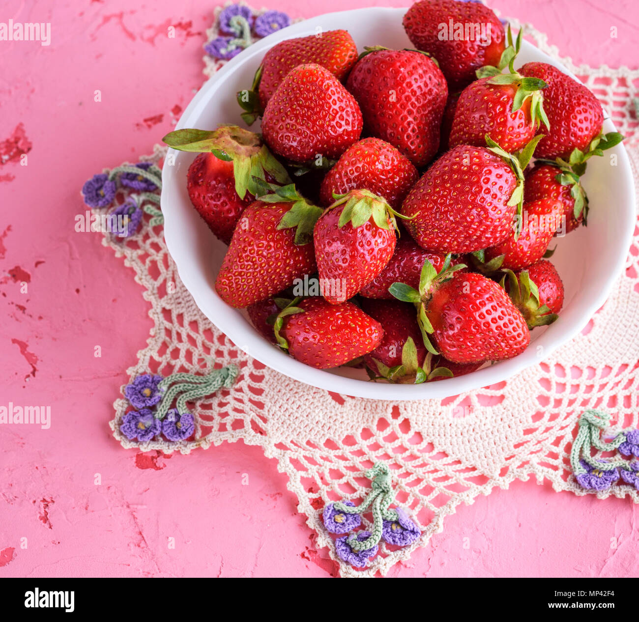 fresh ripe red strawberries in a white round ceramic plate on a pink ...