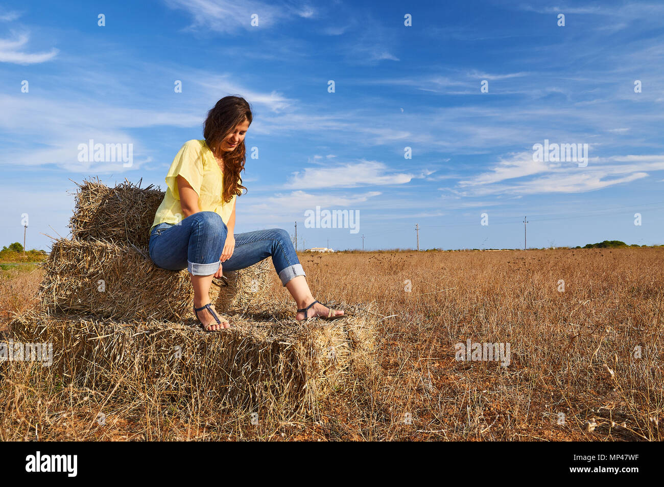 Young woman sitting on a hay bale in a sunny day near El Pilar de la Mola town in Formentera (Balearic Islands, Spain) Stock Photo