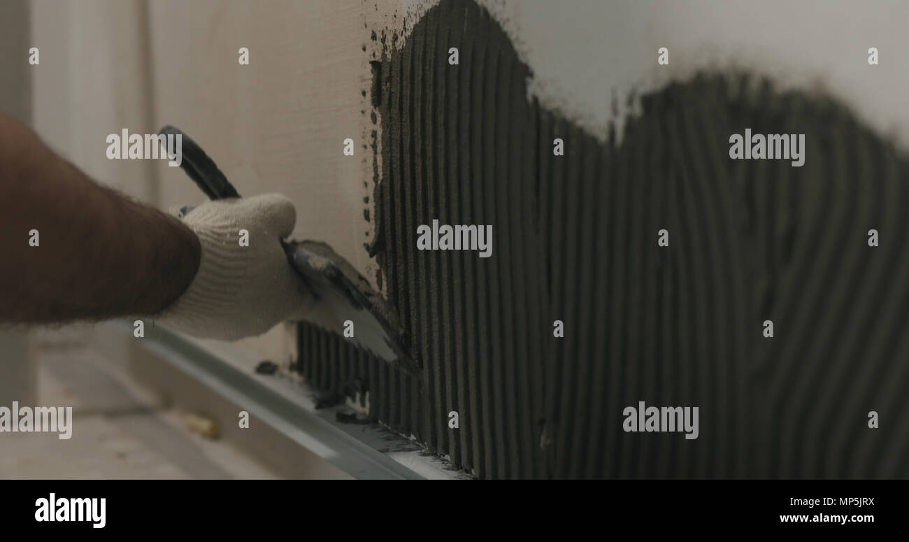 closeup worker applying concrete glue to wall before applying brick tile Stock Photo Alamy