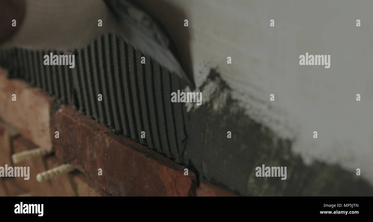 closeup worker applying concrete glue to wall before applying brick tile Stock Photo