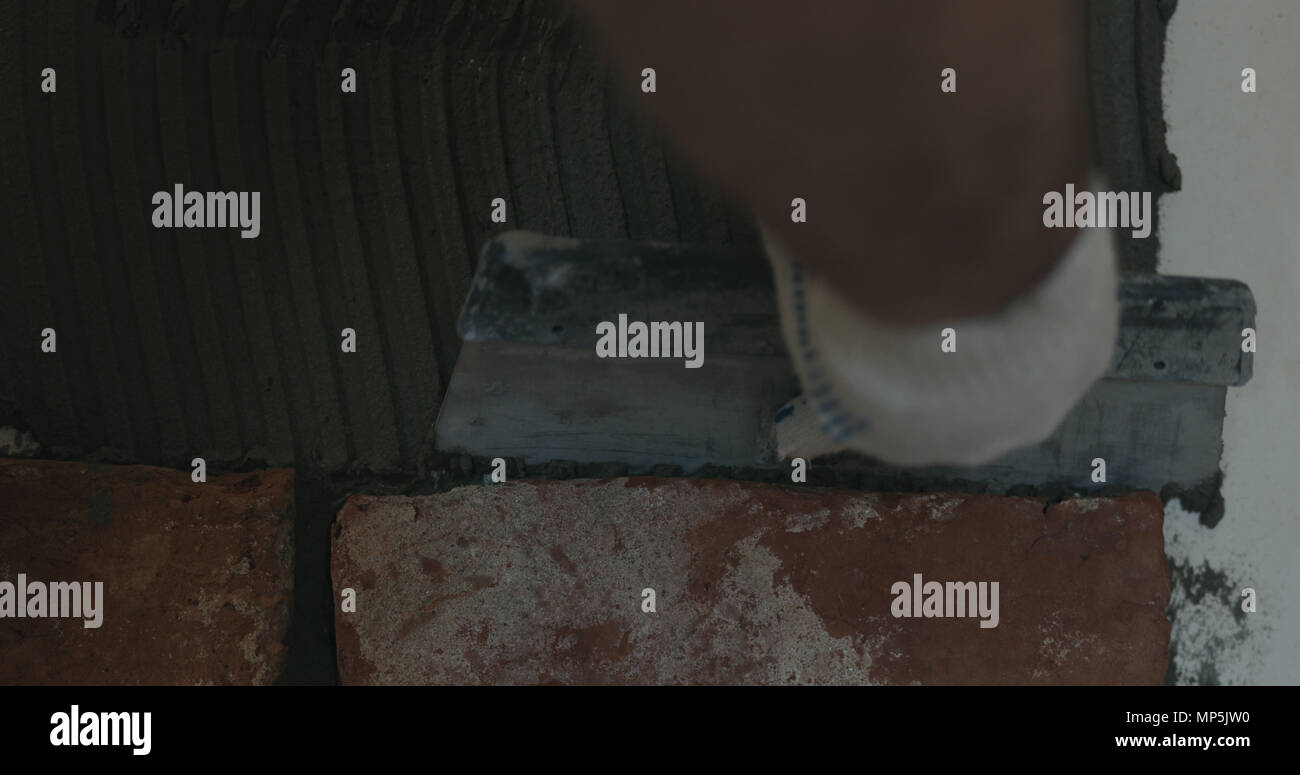 closeup worker applying concrete glue to wall before applying brick tile Stock Photo Alamy